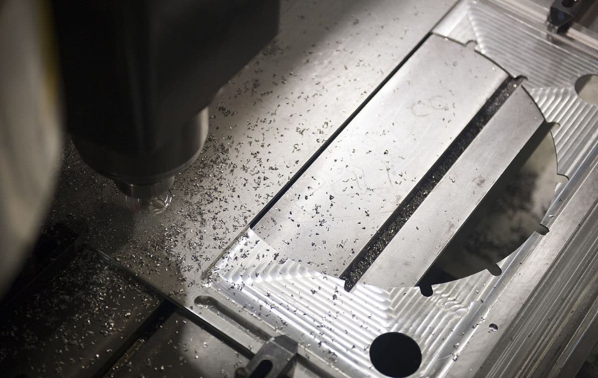 Freshly milled aluminum part in a vise, end mill above it, chips on the table